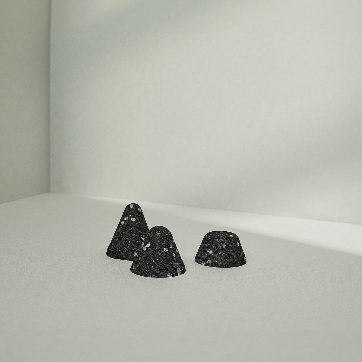 Drei schwarze, kegelförmige Drücker-Aufsätze Mittel von Liebscher & Bracht mit weißen Sprenkeln ruhen auf einer hellgrauen Oberfläche - ideal für Anfänger oder Fortgeschrittene, die eine sanfte Druckstimulation suchen.