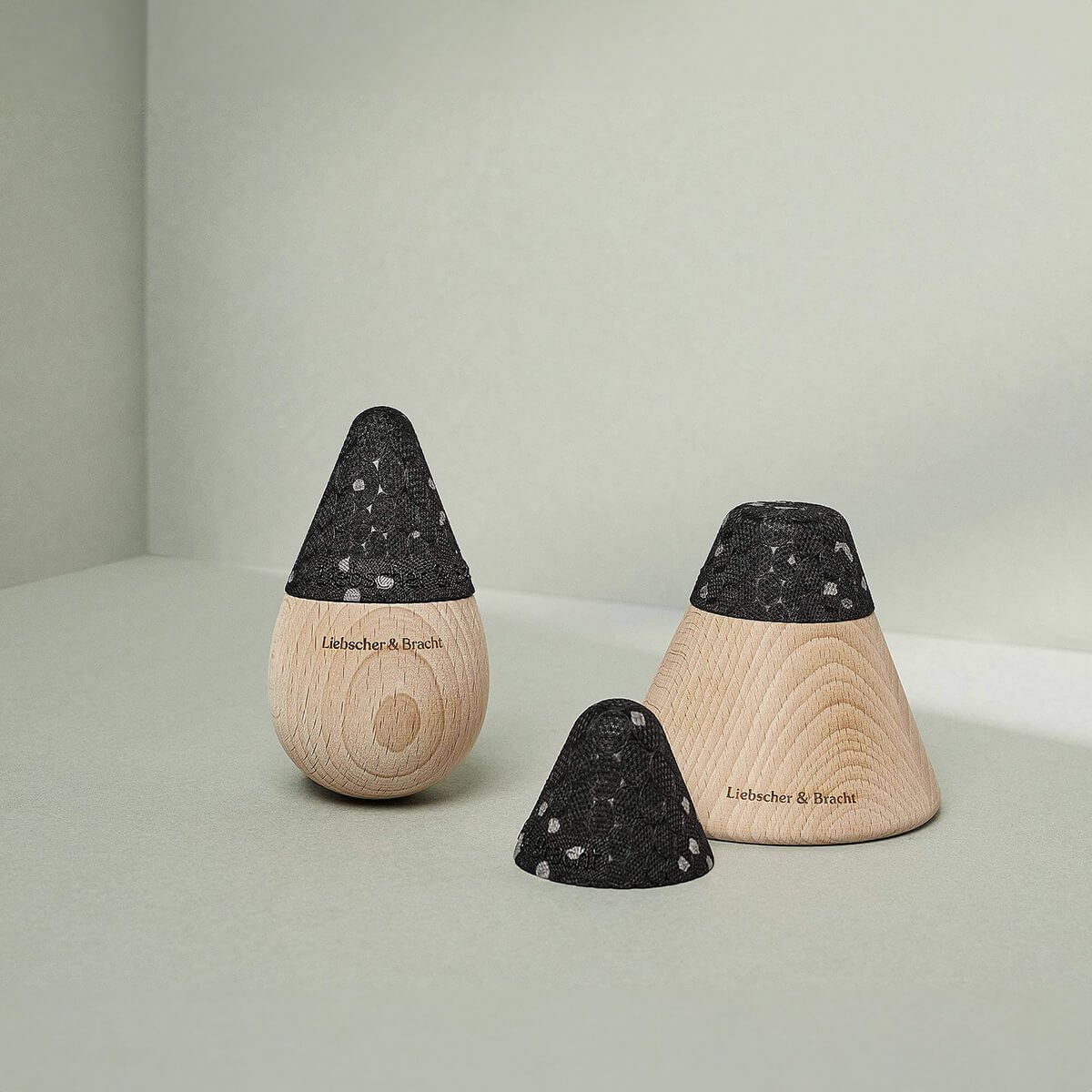 Zwei hölzerne, kegelförmige Liebscher & Bracht Angebots-Pakete mit schwarz gesprenkelter Oberseite sind auf einer hellen Fläche vor einem zartgrünen Hintergrund abgebildet. Ein Deckel ist abgenommen, um das Innere freizulegen, und beide tragen den eingravierten Markennamen.