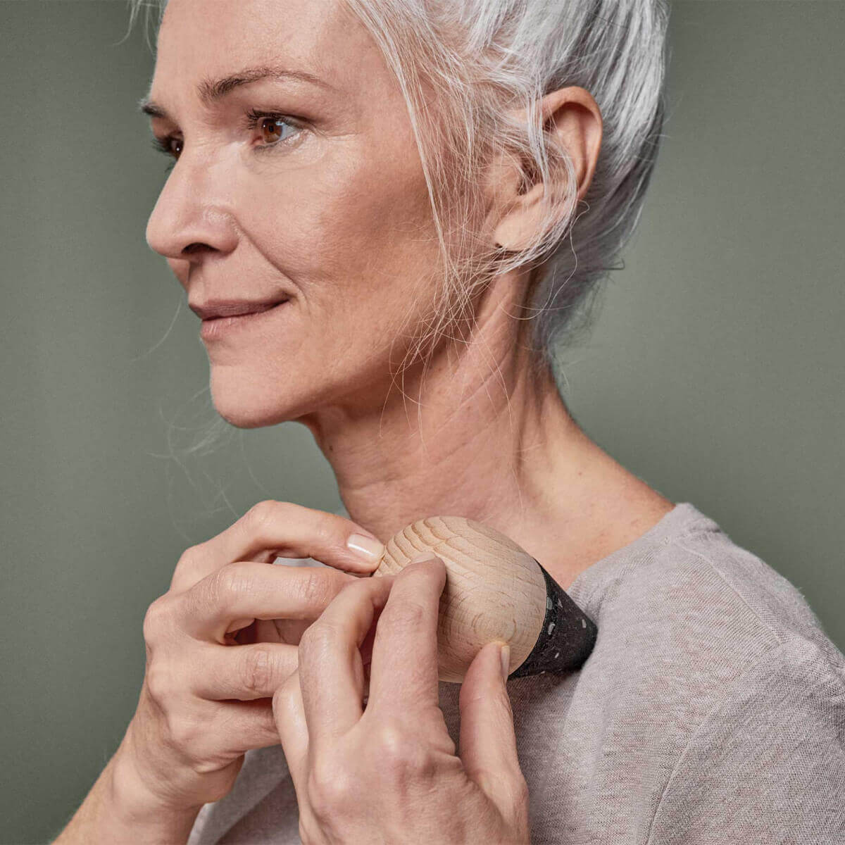 Eine ältere Frau mit grauem Haar trägt das Liebscher & Bracht Schmerzfrei-Drücker-Set auf der Schulter und lächelt sanft in einem hellbeigen Oberteil vor einem neutralen Hintergrund.