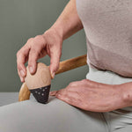 Eine Person in beigefarbenem Hemd und hellgrauer Hose massiert auf einem Stuhl sitzend ihren Oberschenkel mit dem eichelförmigen Werkzeug aus dem Liebscher & Bracht Angebots-Paket Drücker-Set, dessen schwarze Spitze strukturiert ist.