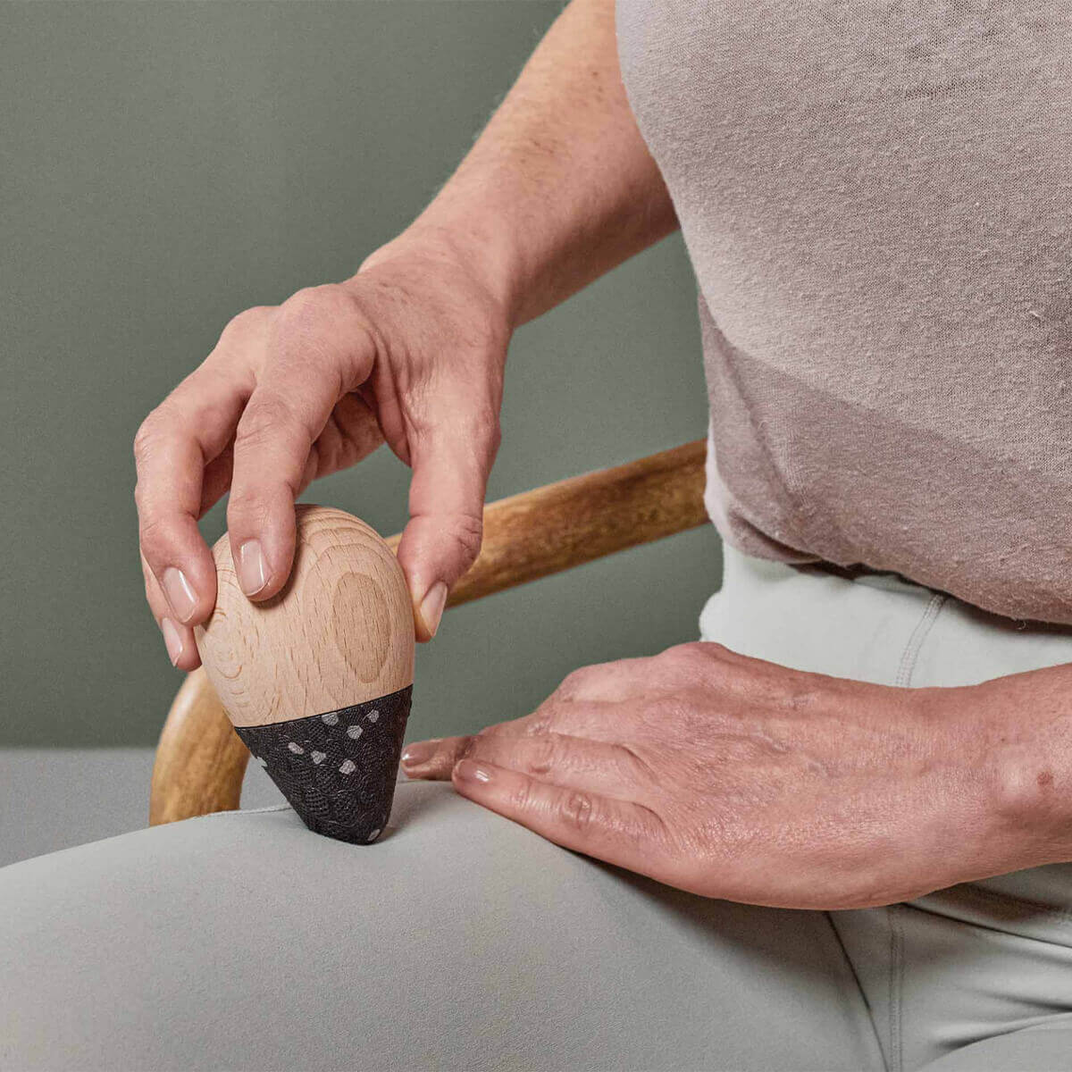 Eine Person in beigefarbenem Hemd und hellgrauer Hose massiert auf einem Stuhl sitzend ihren Oberschenkel mit dem eichelförmigen Werkzeug aus dem Liebscher & Bracht Angebots-Paket Drücker-Set, dessen schwarze Spitze strukturiert ist.