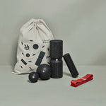 Das Liebscher & Bracht Unsere Empfehlung | Faszien-Set + Übungs-Schlaufe, mit schwarzen Faszienrollen, Massagebällen, rotem Band und beigem Beutel mit schwarzem Print auf grauem Untergrund-ideal für Dehnübungen und Rollmassagen.