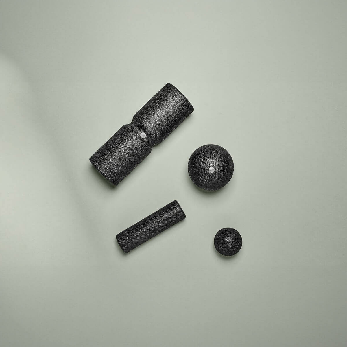 Das Faszien-Rollmassage-Set von Liebscher & Bracht mit vier schwarz strukturierten Werkzeugen - Doppelzylinder, Kugel, kleiner Zylinder und kleine Kugel - liegt auf einer hellgrauen Fläche und unterstützt Beweglichkeit und Entspannung.