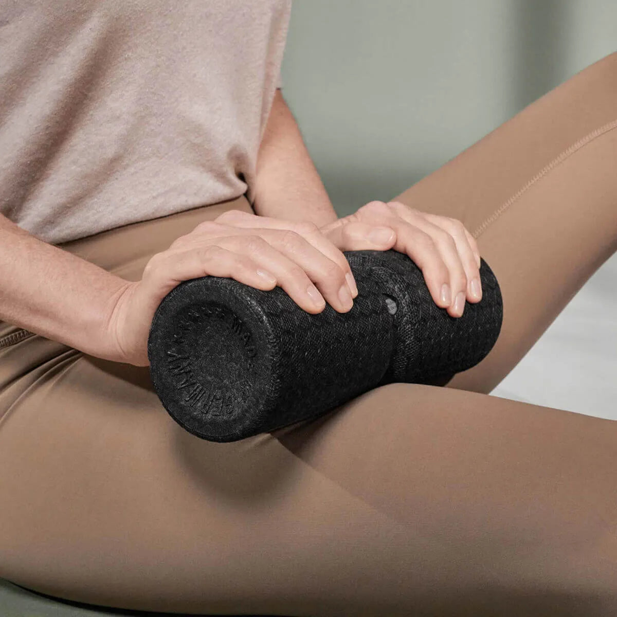 Eine Person in beiger Leggings benutzt die Schaumstoffrolle "Rolle dich schmerzfrei" von Liebscher & Bracht am Oberschenkel und übt mit beiden Händen Druck zur effektiven Faszienentspannung und Selbstbehandlung aus.