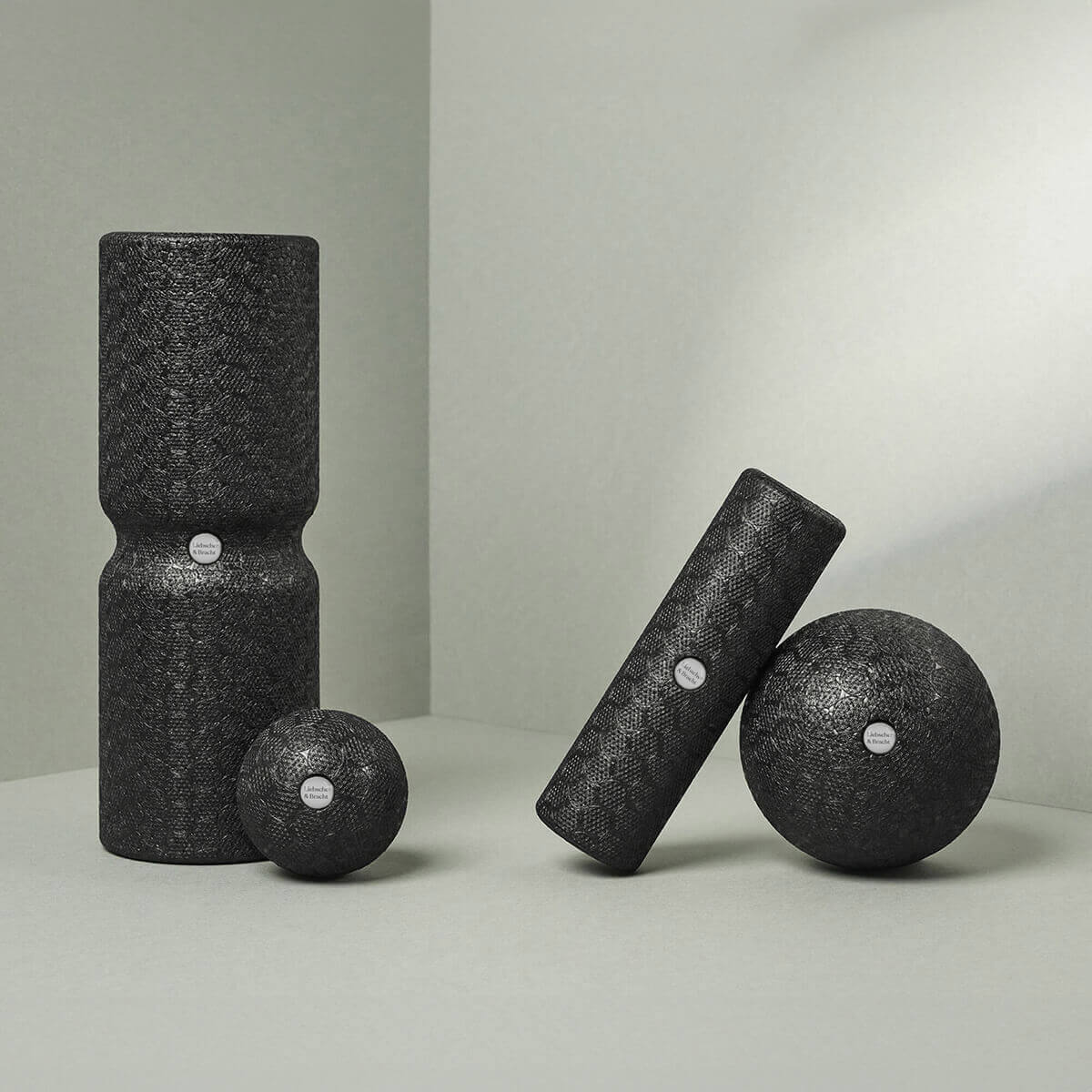 Das Liebscher & Bracht Faszien-Rollmassage-Set besteht aus vier schwarzen Massagerollen und -kugeln in verschiedenen Formen und Größen mit weißer Mittelmarkierung, die auf einer hellgrauen Oberfläche abgebildet sind - ideal zur Entspannung und Verbesserung der Beweglichkeit.