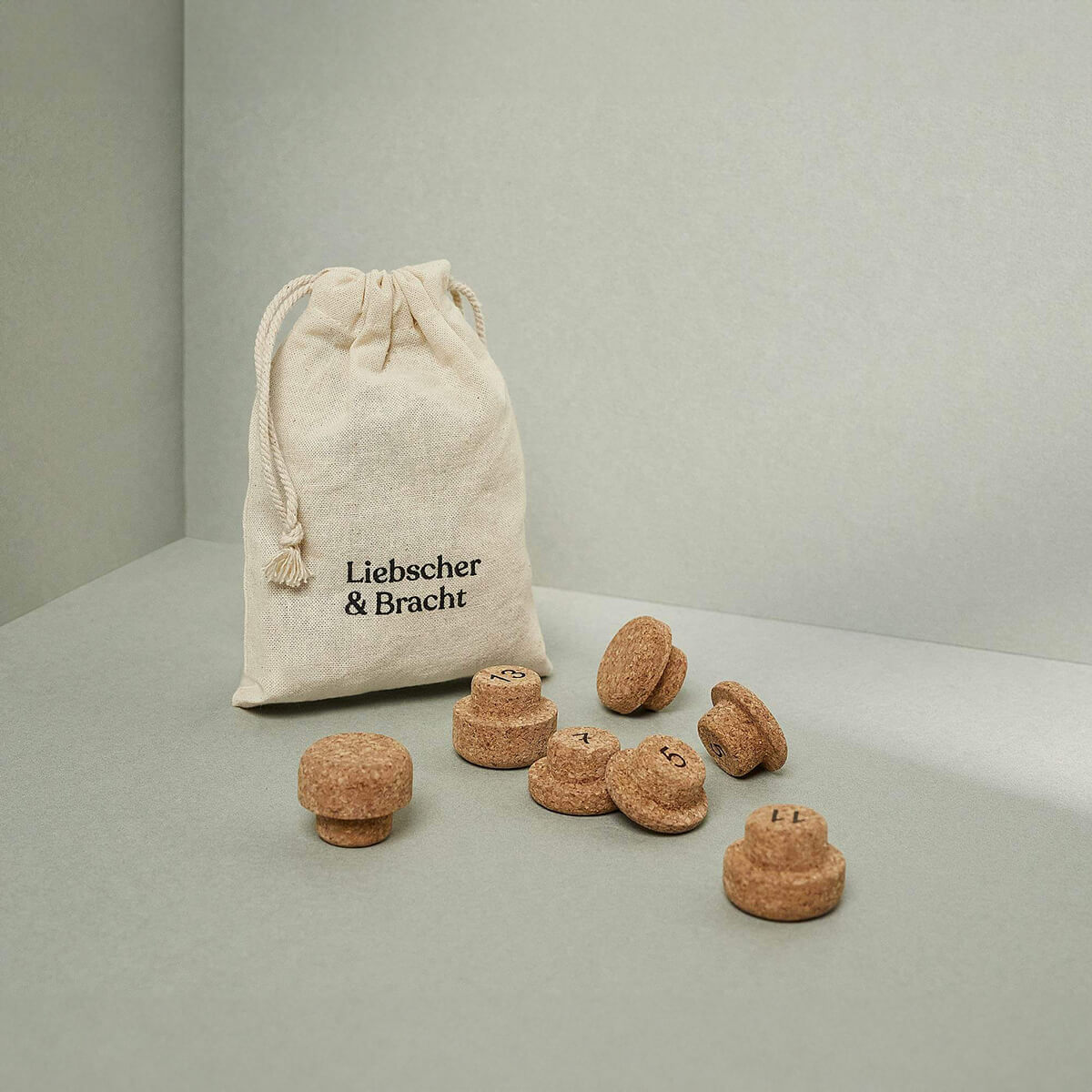 Ein kleiner Liebscher & Bracht-Stoffbeutel ruht auf einer grauen Fläche neben dem Korken-Set für den Kieferretter - verschiedene Massagewerkzeuge in unterschiedlichen Formen und Größen, alle aus nachhaltigem Kork gefertigt.