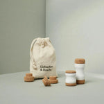 Ein Stoffbeutel mit der Aufschrift Liebscher & Bracht liegt neben dem Kieferretter, einem Set aus weißen Keramikwerkzeugen mit Korkplatten und Scheiben - ideal für Entspannung und Dehnübungen im Kieferbereich, angeordnet auf einer neutralen hellgrauen Fläche.