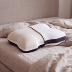 Das Kissen Plus liegt auf einem Bett mit beiger Bettwäsche, die Hülle ist halb übergezogen.