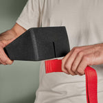 Eine Person fädelt die rote Trittschlaufe durch Der Knieretter mit Trittschlaufe von Liebscher & Bracht - ein schwarzes, keilförmiges Schaumstoffgerät - ideal für Dehn- und Dehnenübungen, dargestellt vor einem schlichten Hintergrund.