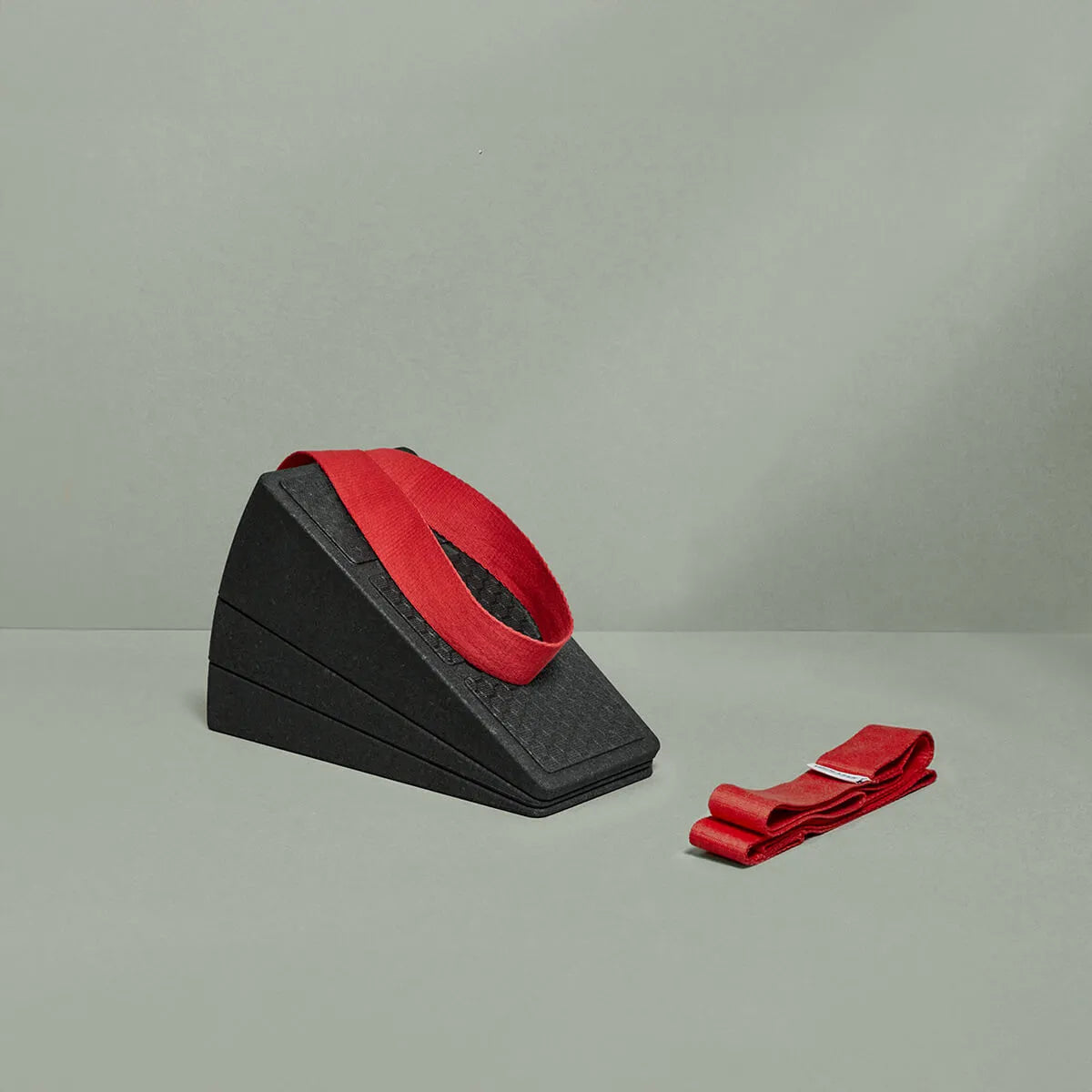 Ein Liebscher & Bracht Knieretter-Set, bestehend aus zwei schwarzen Schaumstoff-Knieretter-Keilen mit einer roten Übungs-Schlaufe darauf und einer weiteren roten Übungs-Schlaufe daneben, wird vor einem schlichten hellgrauen Hintergrund präsentiert.