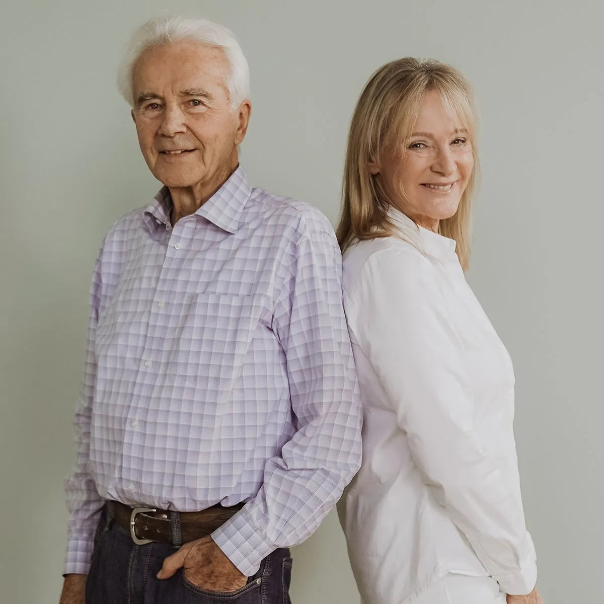 Ein älteres Paar, beide Ernährungsexperten, posiert Rücken an Rücken und lächelt. Sie stehen vor schlichtem Hintergrund und präsentieren das Buch "Klartext Ernährung": Die Antworten auf alle wichtigen Fragen" von Liebscher & Bracht.