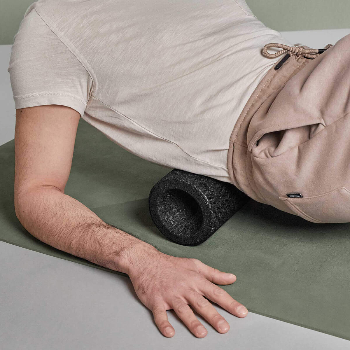 Eine Person in Beige nutzt die Liebscher & Bracht MAXI-Faszienrolle mit Wirbelsäulen-Entlastung in der Seitenlage zur Muskelmassage - ideal für große Körperflächen und zur Unterstützung entlang der Wirbelsäule.