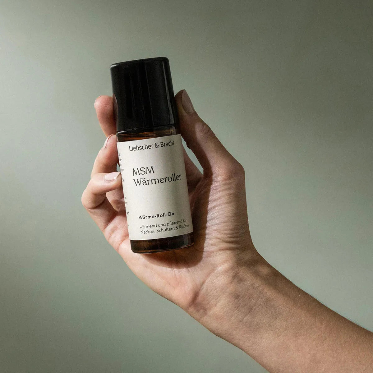 Eine Hand hält eine Flasche des MSM Wärmerollers von Liebscher & Bracht vor einem schlichten, hellen Hintergrund. Der Roll-on unterstützt mit natürlichen Inhaltsstoffen das Wohlbefinden im Nacken, in den Schultern und im Rücken.