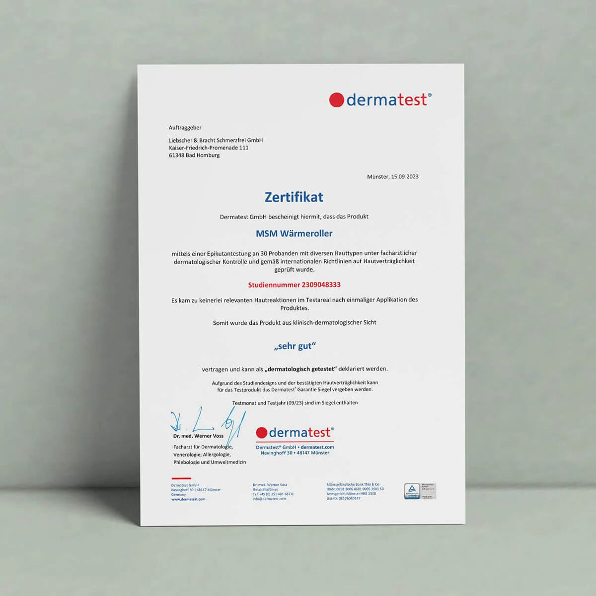 Ein Dermatest-Zertifikat mit Logos und deutschem Text, das hochkant an einer grauen Wand angebracht ist, bestätigt, dass der Liebscher & Bracht MSM Wärmeroller in Bezug auf die dermatologische Sicherheit mit "sehr gut" bewertet wurde (Hautgefühl & Wohlbefinden).