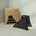 Drei schwarze Der Nackenretter-Schaumstoffkeile in verschiedenen Größen sind vor einer braunen Liebscher & Bracht-Schachtel mit einer Keilabbildung gestapelt - perfekt für Dehnung und vielseitige Anwendungsmöglichkeiten.