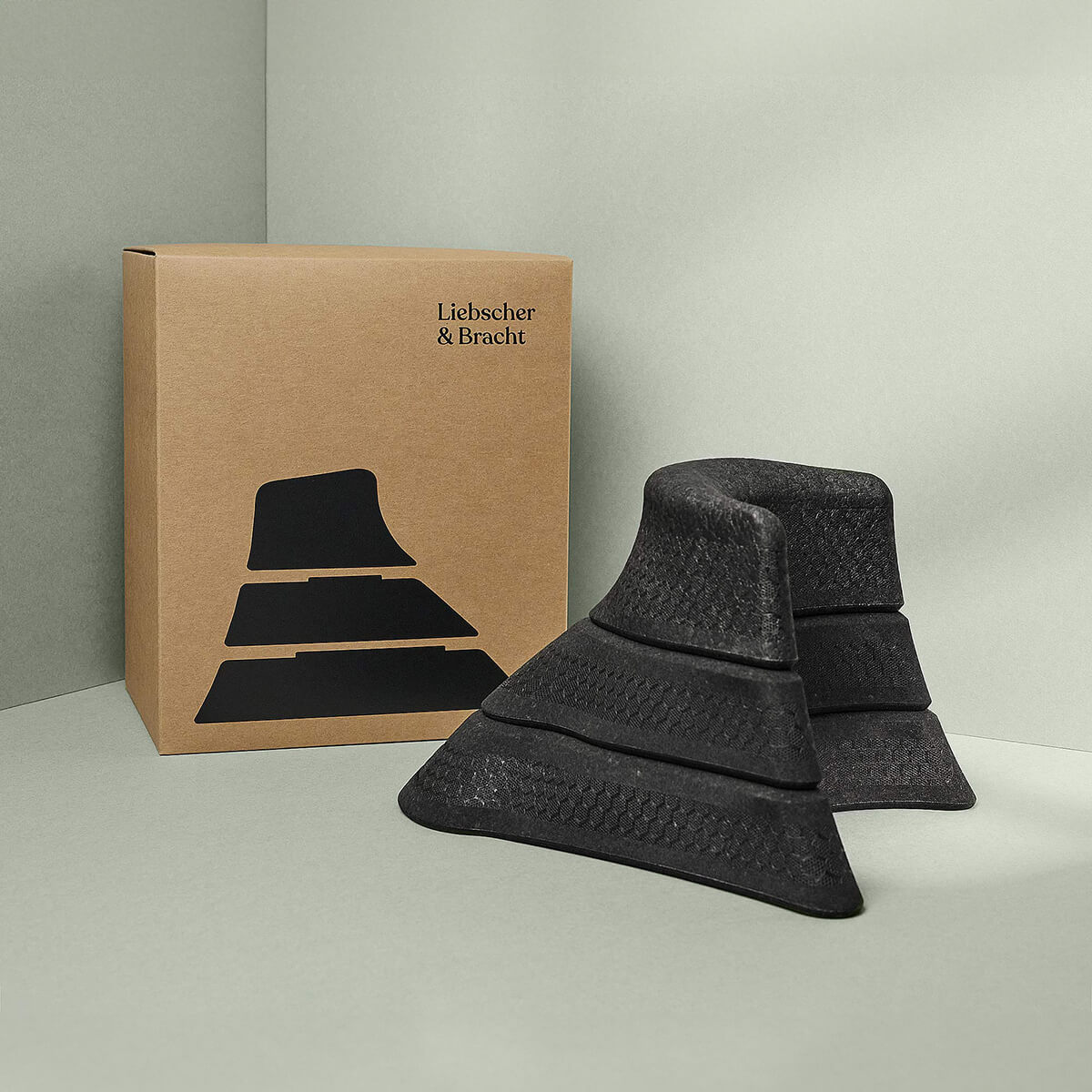 Drei schwarze Der Nackenretter-Schaumstoffkeile in verschiedenen Größen sind vor einer braunen Liebscher & Bracht-Schachtel mit einer Keilabbildung gestapelt - perfekt für Dehnung und vielseitige Anwendungsmöglichkeiten.