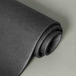 Eine Nahaufnahme einer aufgerollten schwarzen Yogamatte mit einer strukturierten, gerippten Oberfläche auf einem hellgrauen Hintergrund.