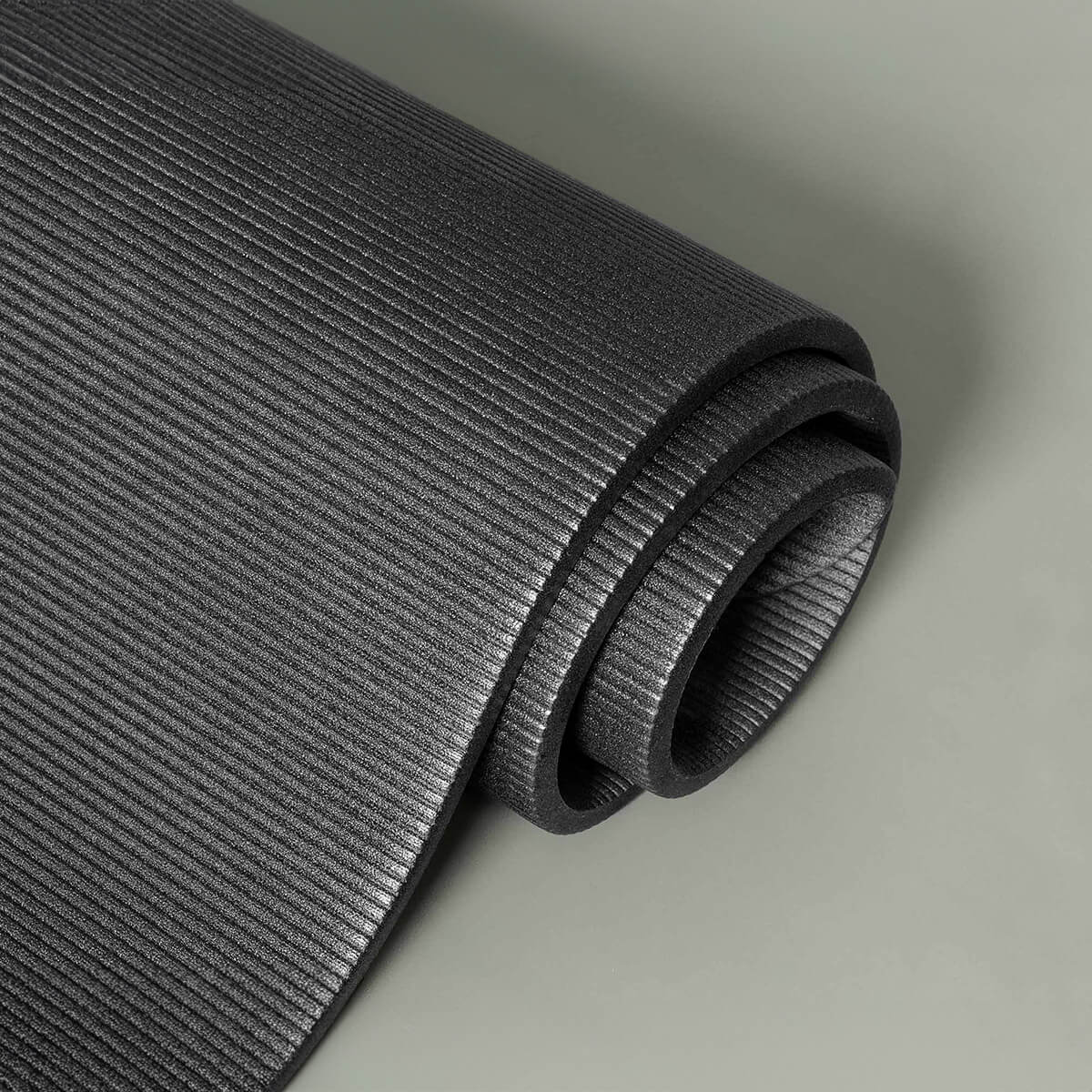 Eine Nahaufnahme einer aufgerollten schwarzen Yogamatte mit einer strukturierten, gerippten Oberfläche auf einem hellgrauen Hintergrund.