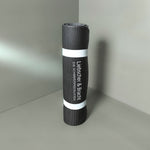 Eine aufgerollte schwarze Gymnastikmatte mit weißer Umrandung, auf der in weißer Schrift der Text Liebscher & Bracht und DIE SCHMERZSPEZIALISTEN zu lesen ist, steht aufrecht in einer Ecke auf einer grauen Fläche.