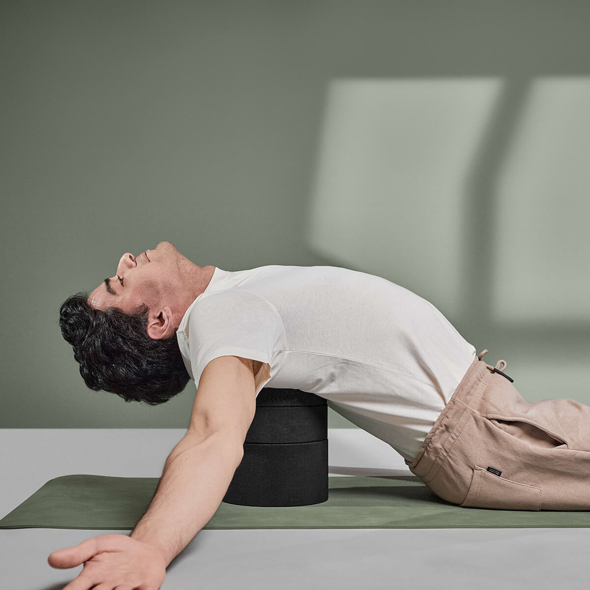 Ein Mann lehnt mit geschlossenen Augen und ausgebreiteten Armen auf dem Liebscher & Bracht Der Rückenretter, der in einer ruhigen Studioumgebung für Mobilisierung und Entspannung der Rückenmuskulatur wirbt.