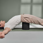 Mit Der Rückenretter von Liebscher & Bracht liegt eine Person auf dem Rücken über zwei schwarzen Yogablöcken mit ausgestreckten Armen auf einer grünen Matte - perfekt für Entspannung und Mobilisierung der Rückenmuskulatur.