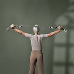 Ein älterer Erwachsener mit kurzen grauen Haaren steht mit erhobenen und ausgestreckten Armen da und hält ein graues Gymnastikband vor einem einfarbig grünen Hintergrund.